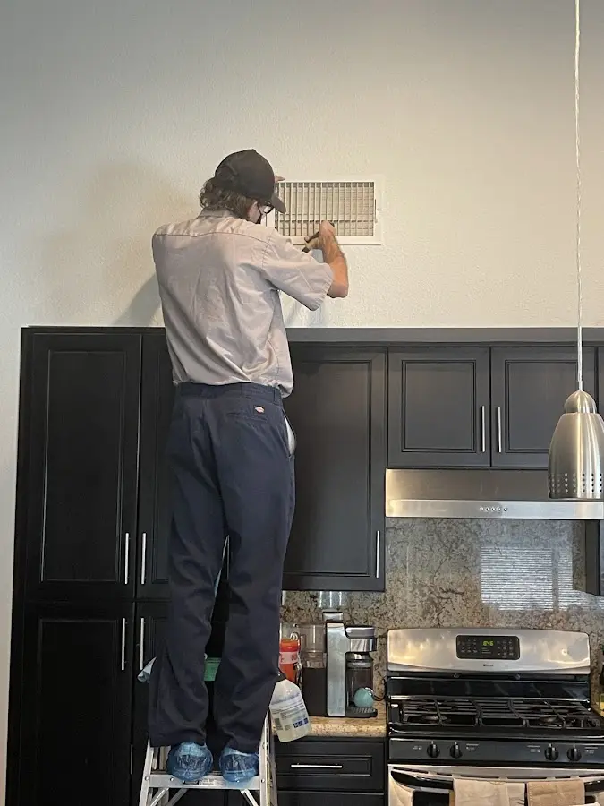 Technician inspecting an air vent during HVAC service in Boulder City